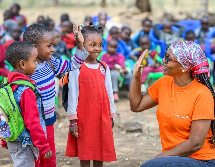 A World Vision staff high-fives three children outside a school in Tanzania.