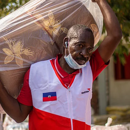 A World Vision staff is carrying a sleeping mat.
