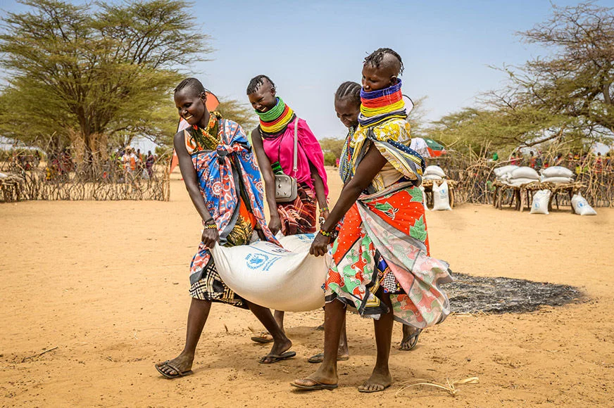 Four women are carrying a sack of food relief during a World Vision distribution program in Kenya. (Kenya, 2022)