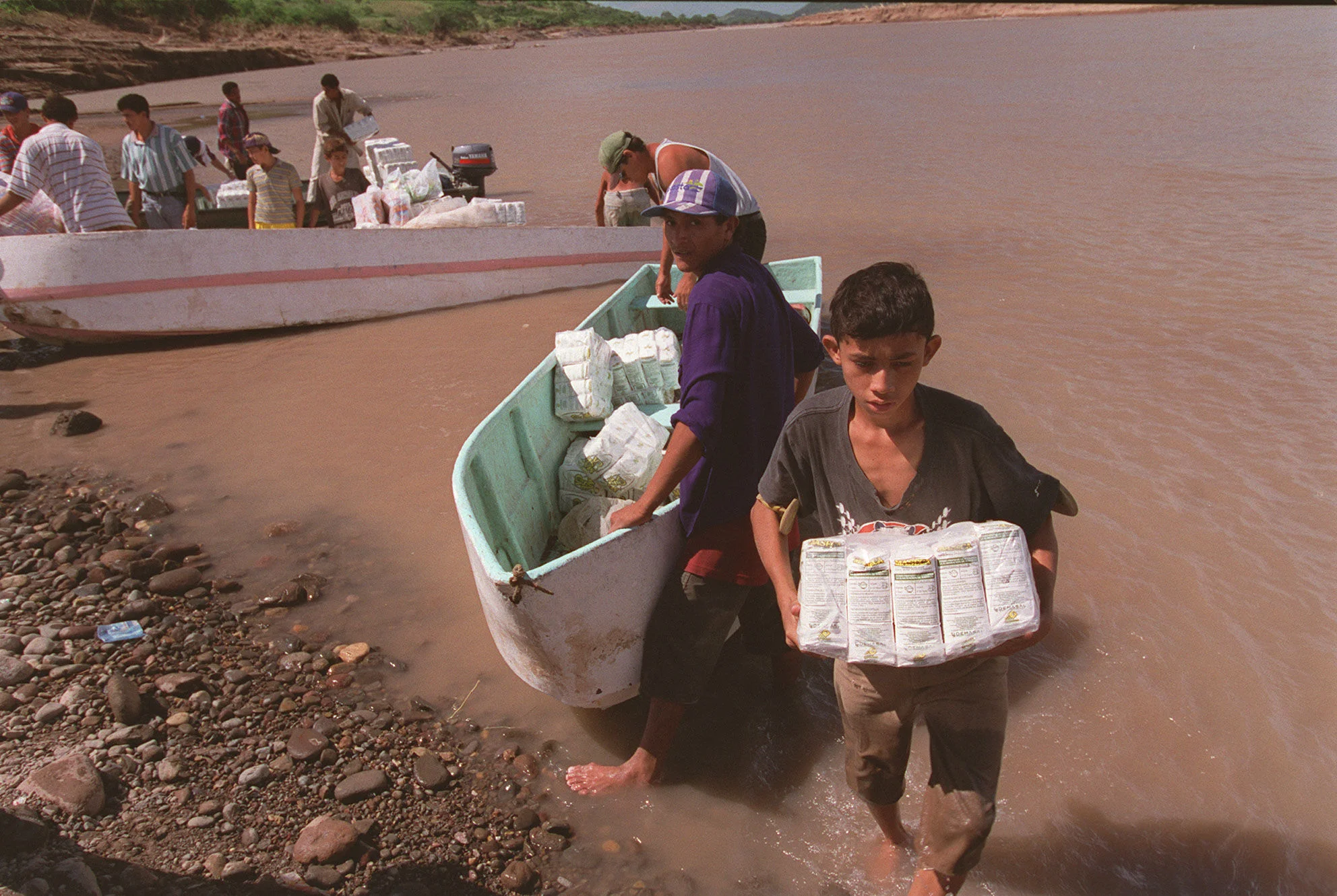 A boy carries provisions from a small boat to the shore. 