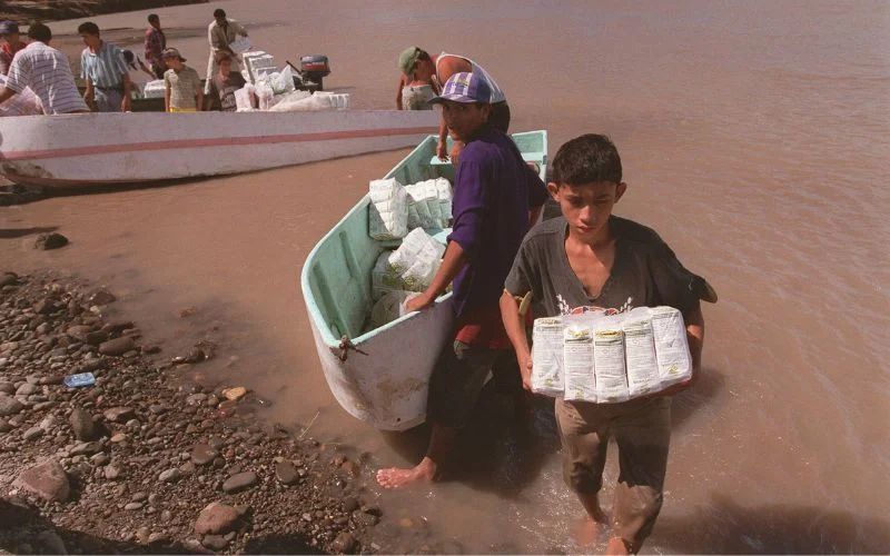 This historical photo shows people in Nicaragua transporting provisions across a river they would normally have crossed by bridge. Hurricane Mitch (1998) destroyed 63 bridges there, separating thousands from food sources and emergency medical care. Photo: Jon Warren