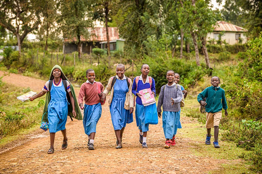 A group of students wearing blue school uniforms are walking in a World Vision area program in Katito, Kenya. (Kenya, 2022)