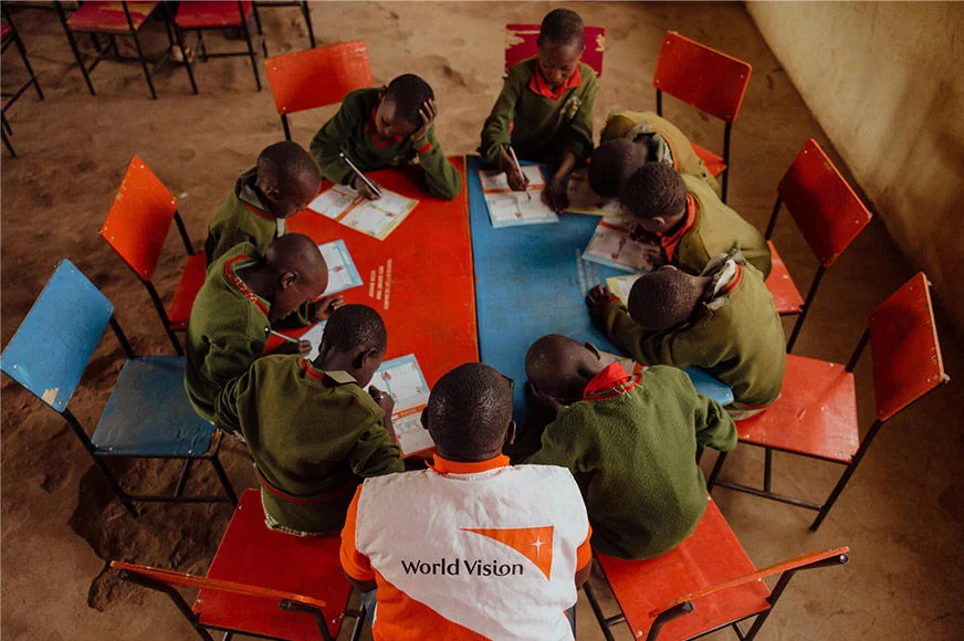 A World Vision staff is facilitating a group of sponsored children in writing letters. (Kenya, 2023)