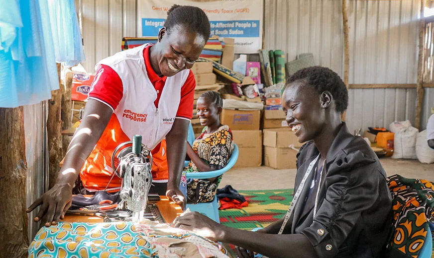 A World Vision staff is helping a woman to sew clothes in a community center.