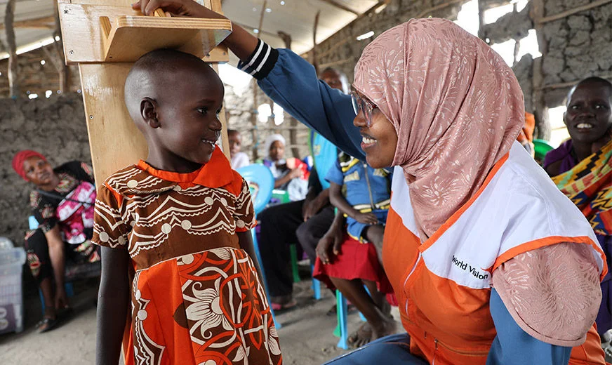A World Vision staff is measuring the height of a child during a health program. (Kenya, 2023)