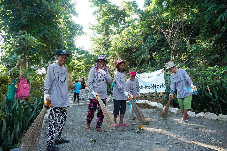 A group of women are sweeping a pathway in a tourist spot in Cagayan, participating in a World Vision cash-for-work program. (Philippines, 2019)